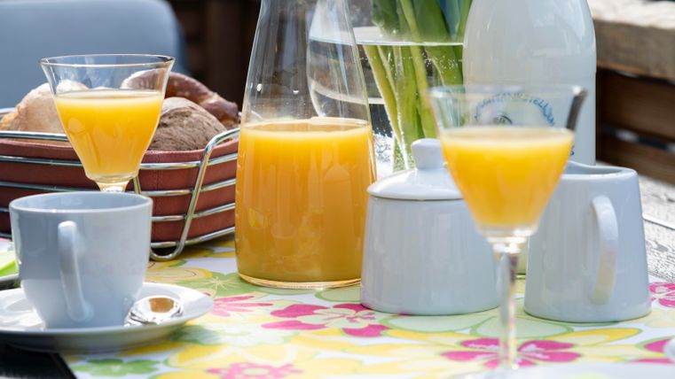 A laid table with fresh fruit juice, coffee, and pastries. The colorful tablecloth creates an inviting atmosphere.