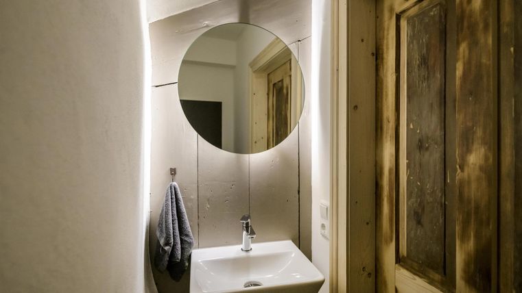 Ein modernes Badezimmer mit einem runden Spiegel und einem Waschbecken. Die Wände sind in neutralen Tönen gehalten und es gibt eine Holzvertäfelung an der Tür.