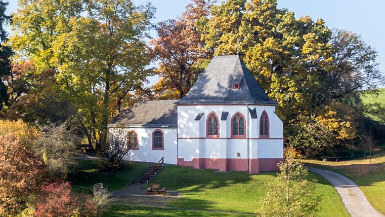 Eine charmante Kirche umgeben von bunten Bäumen im Herbst. Der gepflegte Rasen und der Weg laden zum Wandern ein.