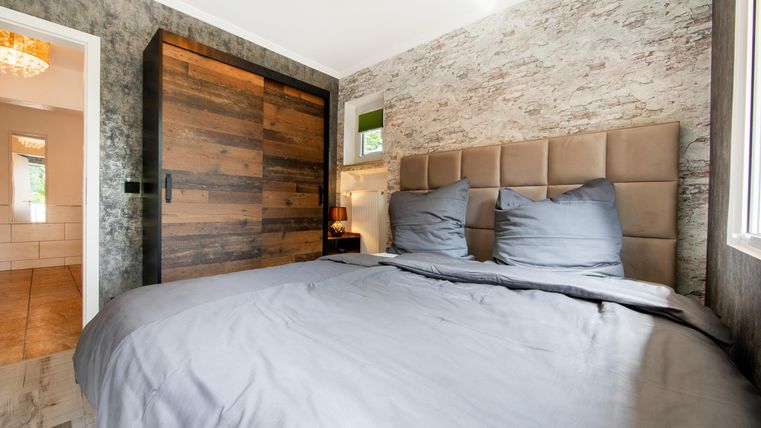 Ein modernes Schlafzimmer mit einem großen Bett und eleganter Bettwäsche. Die Wände sind in warmen, neutralen Tönen gehalten und ein Holzschrank ergänzt die Einrichtung.