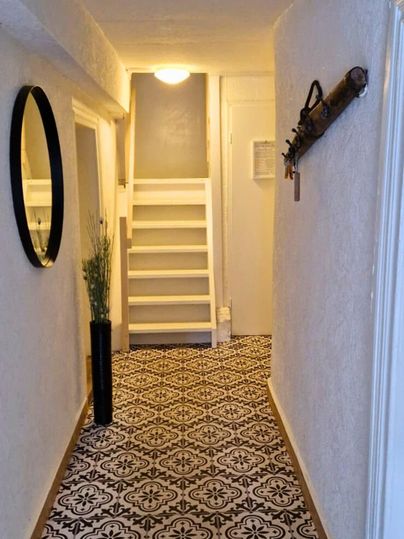 A bright hallway with a colorful patterned floor and a staircase at the end. A mirror and a decorative weapon are hanging on the wall.