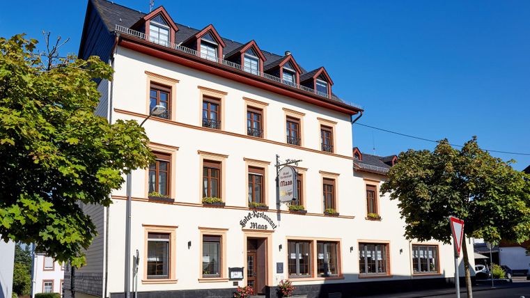 A beautiful historic building with a bright facade and red roof windows. Surrounded by trees and a blue sky.