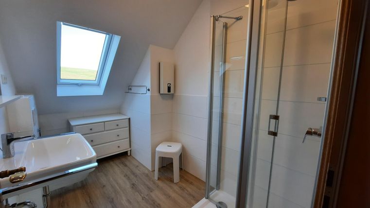 A modern bathroom with a shower and a sink. It has bright walls and plenty of natural light from a skylight.