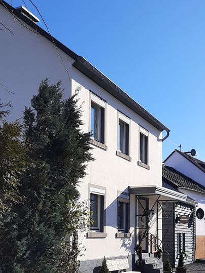 Ein helles Gebäude mit weißen Wänden und großen Fenstern. Der Himmel ist klar und blau, was eine angenehme Atmosphäre schafft.