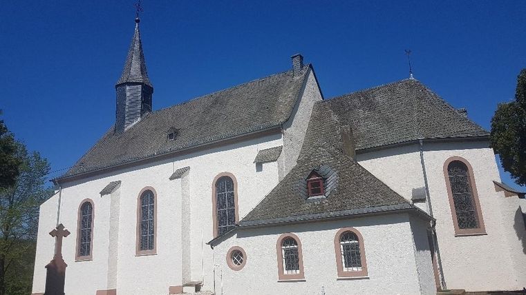 Eine historische Kirche mit einem steilen Dach und einem kleinen Nebengebäude. Der Himmel ist klar und blau, umgeben von grünem Rasen.