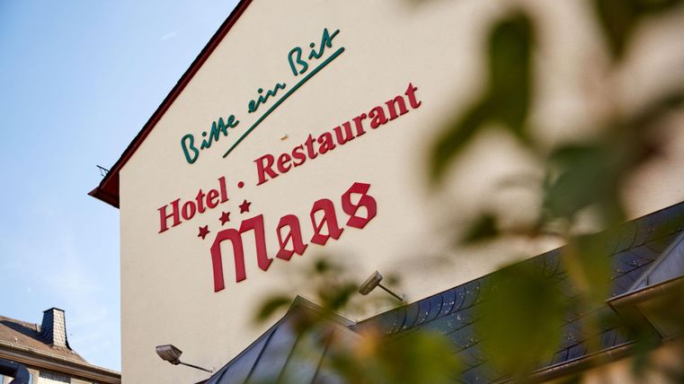 Een hotelgebouw met de opschrift "Hotel - Restaurant Maas". De facade is licht met groene en rode lettertypes.