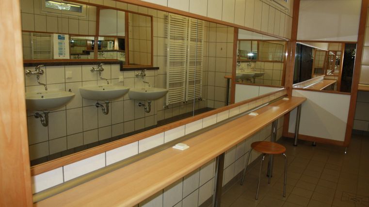 Ein heller, sauberer Waschküchenbereich mit mehreren Waschbecken. An einer langen Holzbank stehen ein paar Stühle.