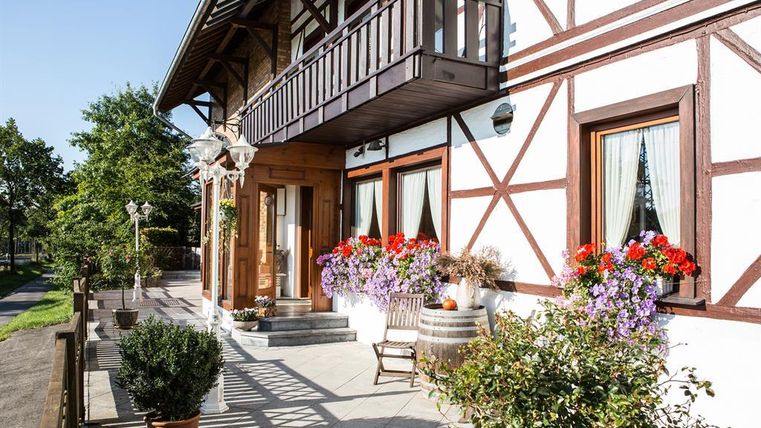 Ein charmantes Fachwerkhaus mit einer einladenden Veranda. Bunte Blumen in Töpfen und ein gemütlicher Holzstuhl gestalten die Atmosphäre freundlich.