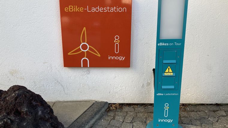 Een eBike-oplaadstation met een informatiebord. Het station is in een stedelijke omgeving geplaatst.