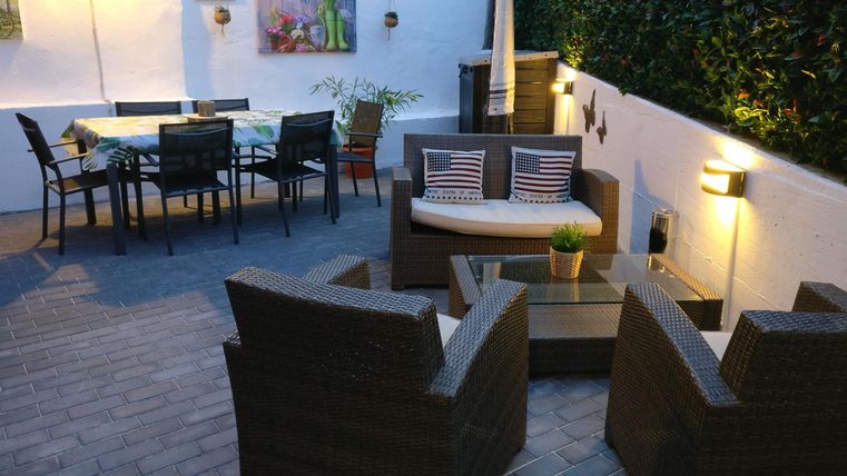 A cozy outdoor area with seating and a dining table. The walls are greened and softly lit.
