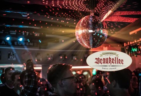 Eine lebhafte Bar mit tanzenden Menschen und einer glitzernden Discokugel. Bunte Lichter schaffen eine festliche Atmosphäre.