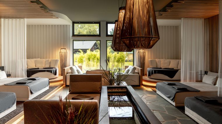 Ein eleganter Wellnessbereich mit komfortablen Liegen und einer ruhigen Atmosphäre. Große Fenster bieten einen Blick auf die grüne Landschaft draußen.