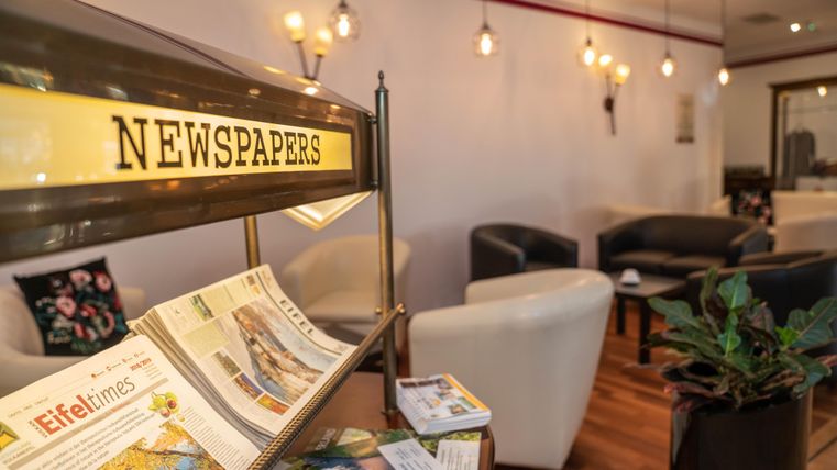 Een gezellige ruimte met comfortabele zitplaatsen en warm licht. Op de voorgrond staat een tijdschriftenhouder met verschillende brochures en catalogi.