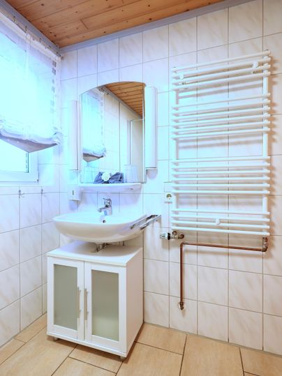 A modern bathroom with a sink and a large mirror. The walls are tiled, and a towel radiator is mounted on the wall.