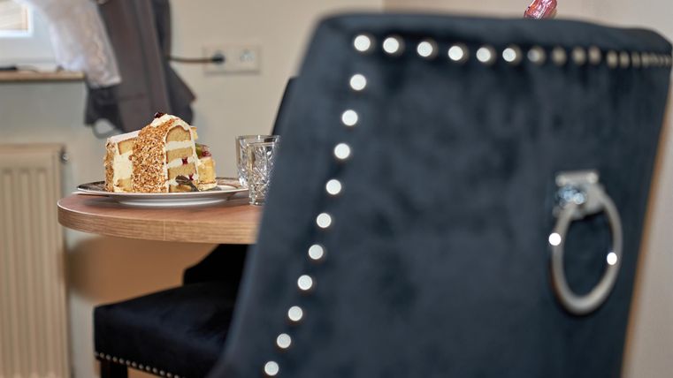A beautiful table with a slice of cake and a glass. In the background, a stylish chair is visible.