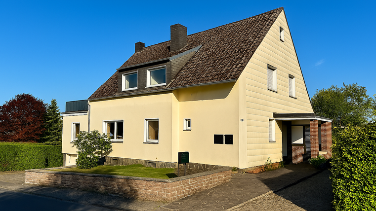 A beautiful single-family house in yellow with a sloping roof and green plantings. The sky is clear and blue.