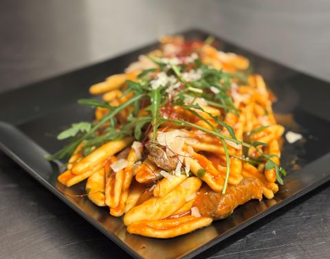 Een bord met frietjes, gegarneerd met stukjes vlees en verse kruiden. Het gerecht is versierd met een rode saus.