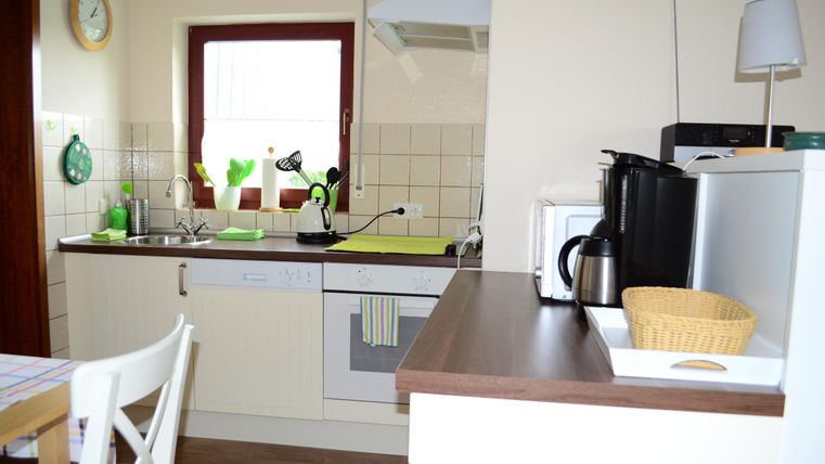 A bright kitchen with modern appliances and a tidy layout. On the countertop, there is a coffee pot and a fruit bowl.