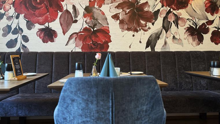 Een modern restaurant met een elegante muurschildering van rode bloemen. De inrichting is gezellig met blauwe banken en stijlvolle tafeldecoraties.