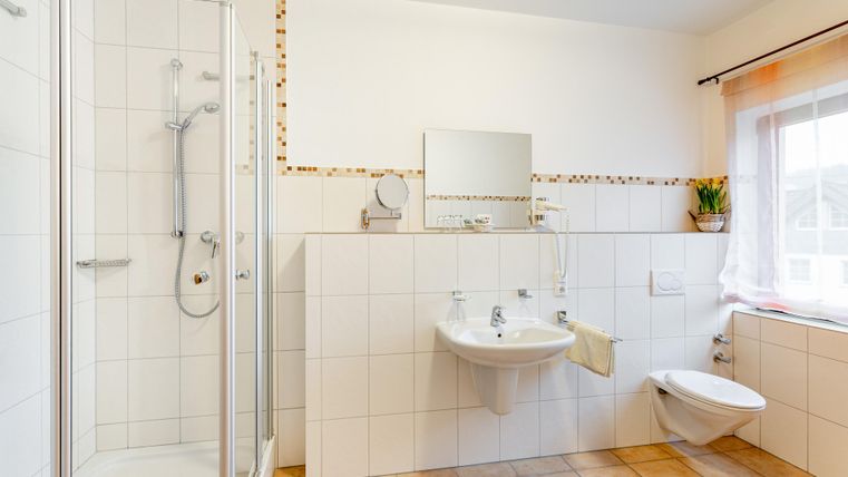 Een moderne badkamer met douche, wastafel en wc. De ruimte is licht en vriendelijk ingericht, met tegels op de vloer en een raam.