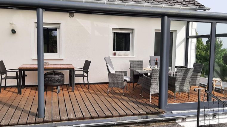 Eine moderne Terrasse mit Holzboden und einem Glasschutz. Es gibt mehrere Tische und Stühle, die zu einem gemütlichen Essen einladen.