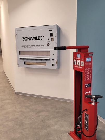 Een fietsreparatiestation met een luchtpomp en een gereedschapsset aan de wand. Het station is geïnstalleerd in een moderne, lichte ruimte.