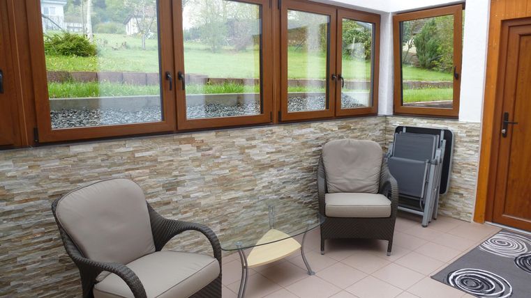 Ein gemütlicher Raum mit zwei Sessel und einem kleinen Tisch. Große Fenster bieten einen Blick ins Grüne.