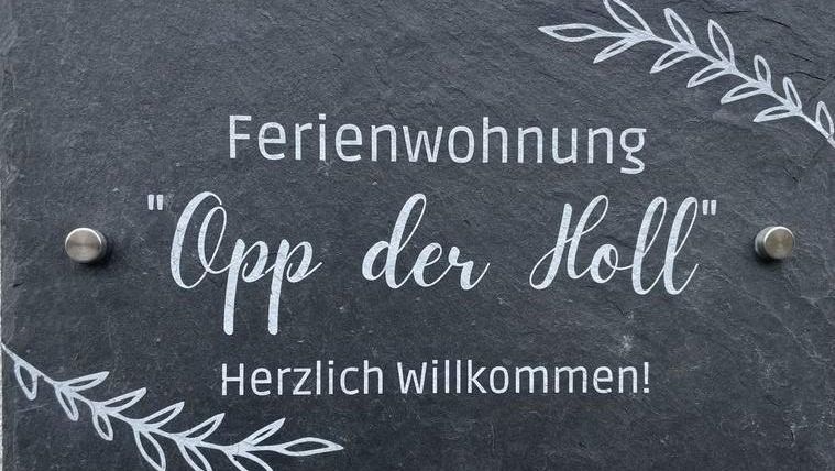 Een bord voor een vakantiehuis met de naam "Opp der Holl". Het zegt "Hartelijk Welkom!" en heeft een decoratief lettertype en plantenmotieven.