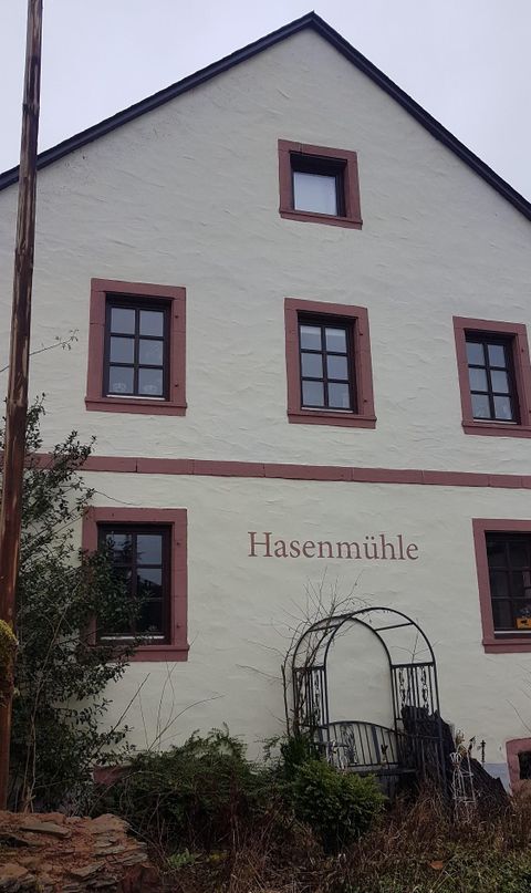Ein charmantes Gebäude mit dem Namen "Hasenmühle". Es hat mehrere Fenster und ist von grünen Pflanzen umgeben.