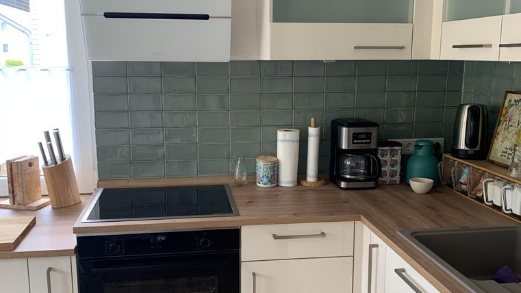 Een moderne keuken met witte kasten en een houten werkblad. In de hoek staat een koffiezetapparaat en het raam laat veel licht binnen.