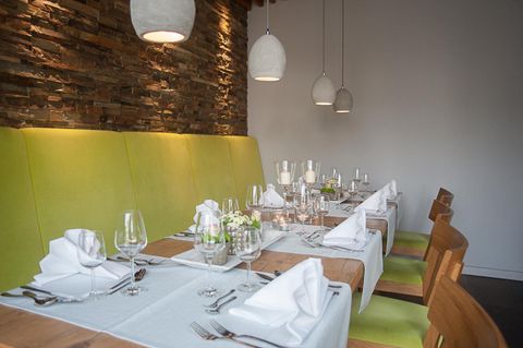 An elegant restaurant with a long table that is stylishly set. The walls are clad in natural stone, and the seats are in a fresh green tone.