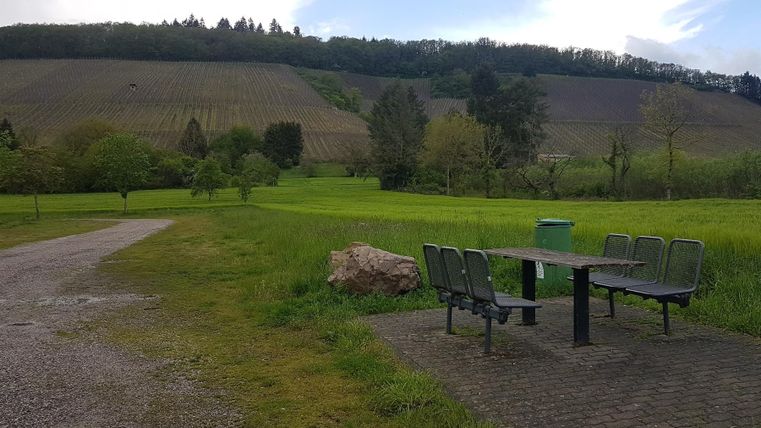 Ein ruhiger Platz im Grünen mit einem Tisch und Stühlen. Im Hintergrund sieht man Weinberge und sanfte Hügel.