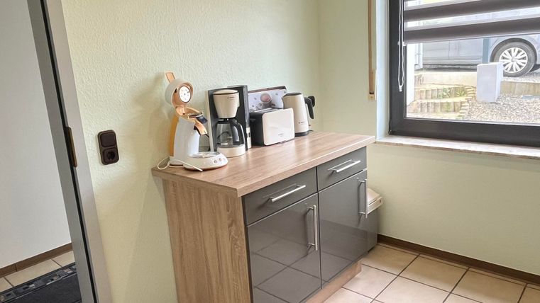 A modern kitchen with a wooden cabinet and various kitchen appliances. The window provides lots of daylight and a view outside.