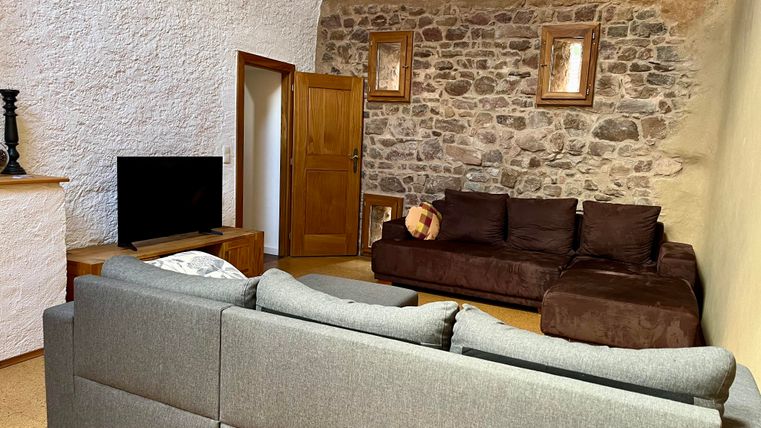 Ein gemütliches Wohnzimmer mit einer grauen Sofalandschaft und einem braunen Sofa. An der Wand befindet sich eine Steinmauer und dekorative Bilder.