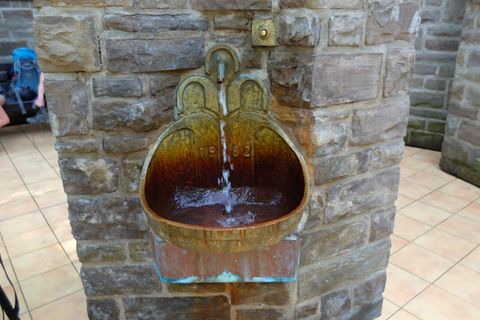 Een antieke metalen fontein met stromend water. De fontein is geïntegreerd in een stenen muur.