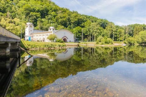 Een rustige vijver met een heldere weerspiegeling van de omliggende natuur. Op de achtergrond is een historisch gebouw en weelderig groen te zien.