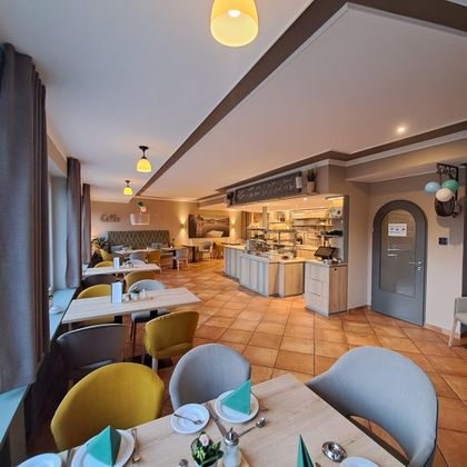 A modern restaurant with bright walls and cozy tables. There are benches and chairs in various colors as well as an open kitchen.