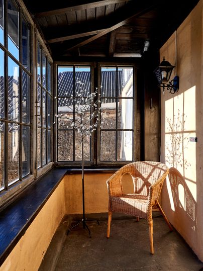 A cozy porch with large windows and a wicker chair. The light gently falls on the floor and the walls.