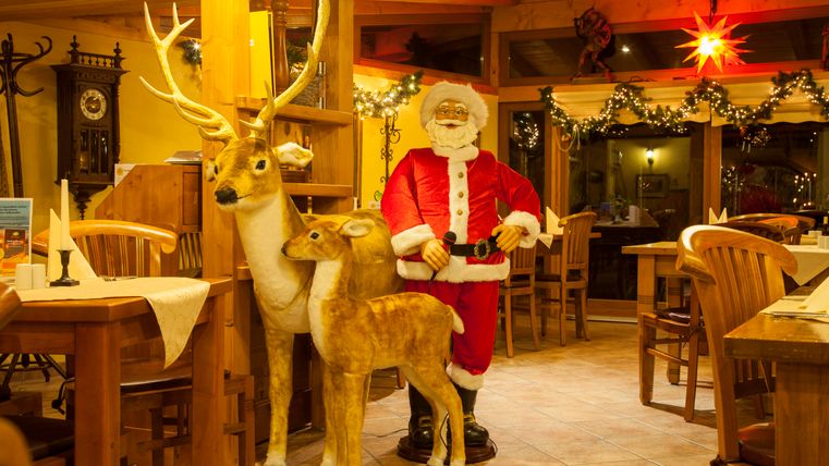 Ein festlich dekoriertes Restaurant mit einem Weihnachtsmann und zwei Holzrehen. Die gemütliche Atmosphäre wird durch die Lichter und Dekorationen unterstrichen.