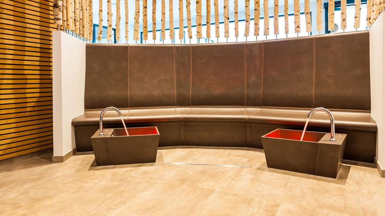 Ein eleganter Wellnessbereich mit einer halbkreisförmigen Bank und zwei Waschbecken. Der Raum hat eine moderne Holzverkleidung und einen hellen Boden.