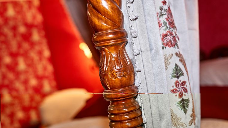 A decorative headboard made of wood with a twisted column. In the background, red walls and a bed are visible.
