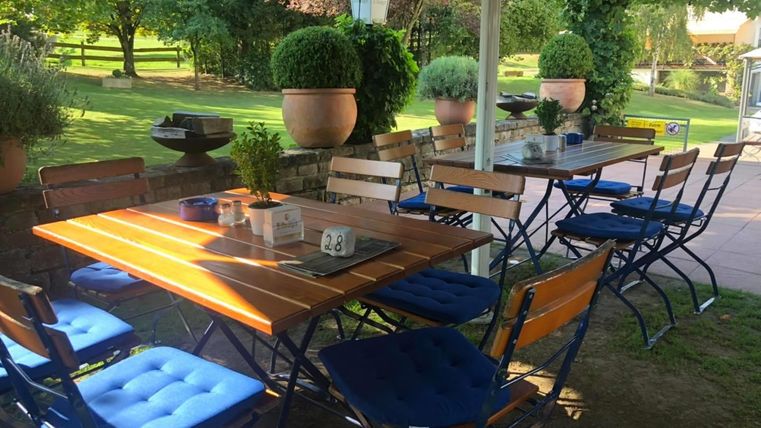 Ein einladender Außenbereich mit einem Tisch und Stühlen. Im Hintergrund sind grüne Bäume und Pflanzen zu sehen.