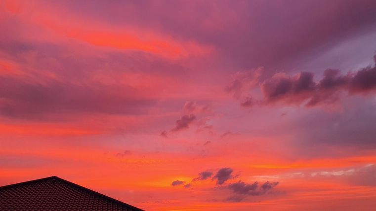 Ein schöner Sonnenuntergang mit leuchtenden Rosa- und Orangetönen. Im Vordergrund ist ein Dach eines Hauses sichtbar.