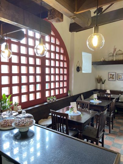 Ein gemütliches Café mit Holztischen und Stühlen. Große Fenster bieten viel Tageslicht und eine einladende Atmosphäre.