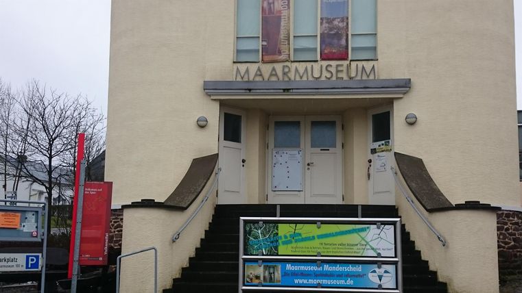 Ein Gebäude mit dem Schriftzug "MAARMUSEUM" über dem Eingang. Es gibt Treppen und Informationsschilder im Vordergrund.