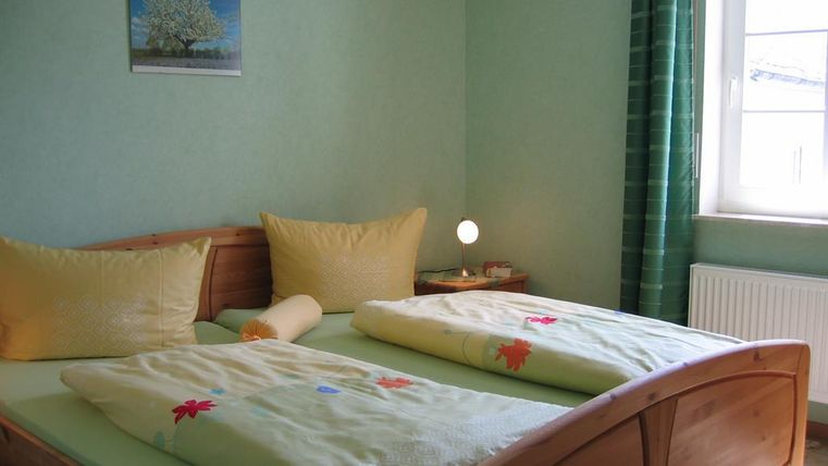 Ein gemütliches Schlafzimmer mit einem Doppelbett und schönen Kissen. Die Wände sind in einem sanften Grün gestrichen und das Fenster lässt viel Tageslicht herein.