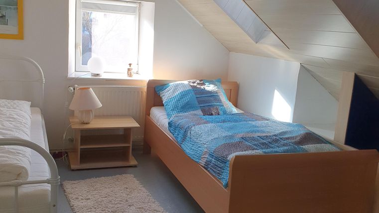 Een lichte slaapkamer met twee bedden en een rustige sfeer. Een raam zorgt voor natuurlijk licht en de inrichting is eenvoudig en functioneel.