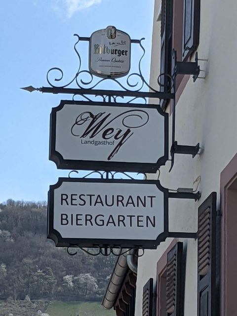 Ein Schild mit den Aufschriften "Wey Landgasthof" und "Restaurant Biergarten". Es hängt an einer Wand und zeigt eine gemütliche Gaststätte.
