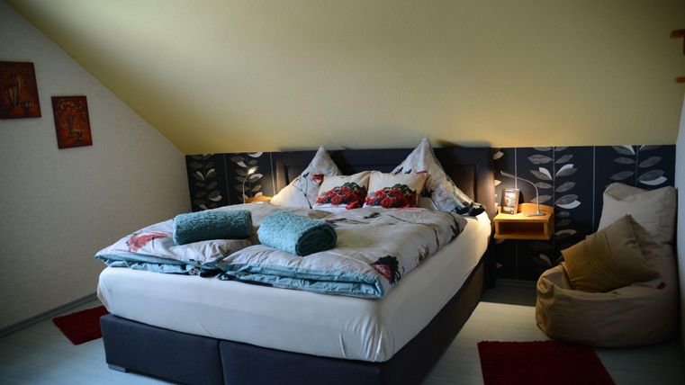 Een gezellige slaapkamer met een groot bed, decoratieve kussens en zacht licht. Een hoek met een zitzak en stijlvolle wanddecoraties zorgt voor een uitnodigende sfeer.