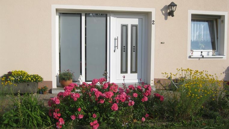 Ein schöner Hauseingang mit einer modernen Tür und bunten Blumen im Garten. Die Pflanzen verleihen dem Eingang einladende Farben und eine freundliche Atmosphäre.